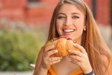 Woman eating tasty croissant in cafe outdoors