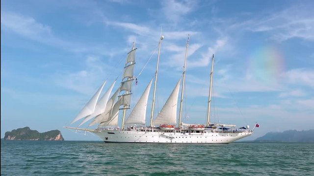 Luxurious white tall ship with masts or brigantine sailing in tropical sea against rocky islands or cliffs and beautiful sky with clouds on background. Touristic vessel or cruise yacht. Thailand.
