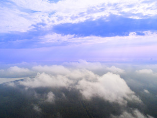 Naklejka na ściany i meble Aerial Drone view clouds over the green forest and lake. Low lying cloud. Aerial view of over tropical rainforest. Above the clouds in the sky. Big clouds. Atmosphere. Top view from drone