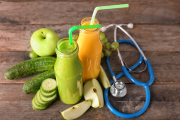 Bottles of tasty smoothies with ingredients and stethoscope on wooden table. Diet concept