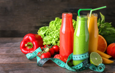 Bottles of tasty smoothies with ingredients and measuring tape on wooden table. Diet concept