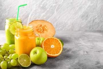 Mason jars of tasty smoothies with fruits on grey table