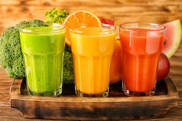 Glasses of tasty smoothies with ingredients on wooden board