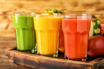 Glasses of tasty smoothies with ingredients on wooden board