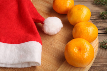 Fresh mandarins or tangerines on the wooden table with Xmas tree branches and hat of Santa Claus