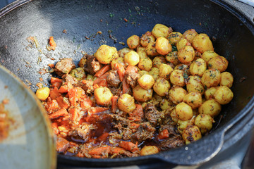 Roast meat and potatoes cooked in a large open-air boiler.