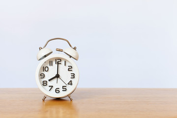 White alarm clock on wooden table with white wall background. Front view and copy space