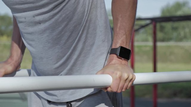 Professional mature athlete doing push-ups on parallel bars wearing smartwatches