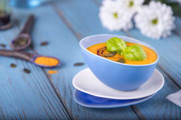 Pumpkin cream soup with pumpkin seeds, pumpkin oil and turmeric on a blue background