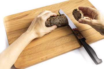 woman cutting with a knife a small loaf of wholemeal bread with freshly made walnuts on a wooden board
