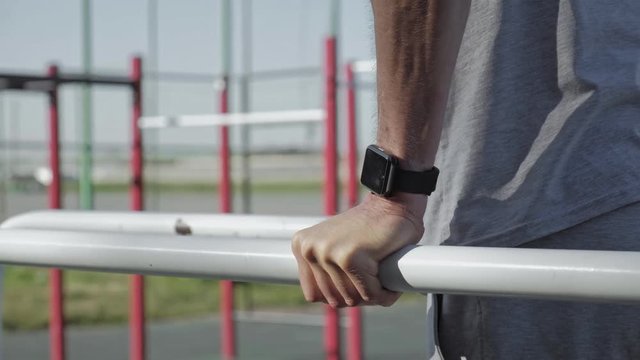 Professional adult athlete doing push-ups on parallel bars wearing smartwatches.