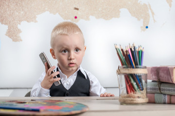 Малыш сидит за школьной партой с телефоном в руке 