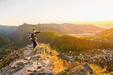 Young traveler stands on a stone and points the finger forward against the background of the mountains.