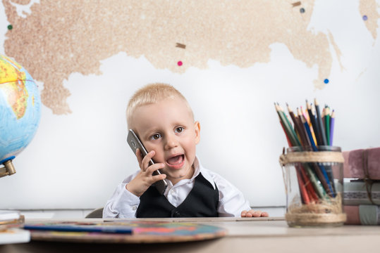 Малыш сидит за школьной партой с телефоном в руке 