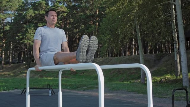 Athletic man doing gymnastic exercise on parallel bars wearing smartwatches.