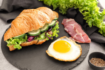 Tasty croissant sandwich with fried egg on slate plate