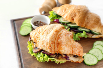 Tasty croissant sandwiches on wooden board