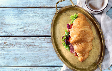 Tasty croissant sandwich with meat on metal tray