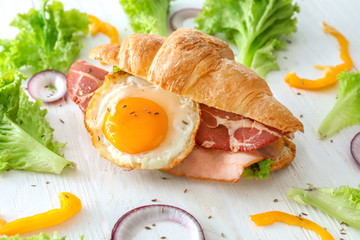 Tasty croissant sandwich with fried egg on white wooden table