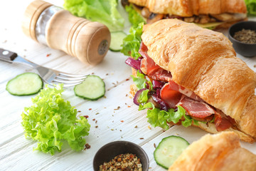Tasty croissant sandwich with meat on white wooden table