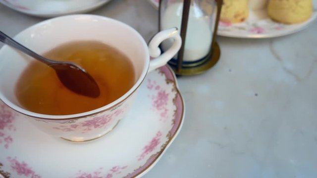 Hand is using stainless steel to stir english tea in the beautiful english tea cup with background of sweet dessert (scone)