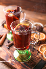 Glass cups of delicious hot mulled wine on wooden board