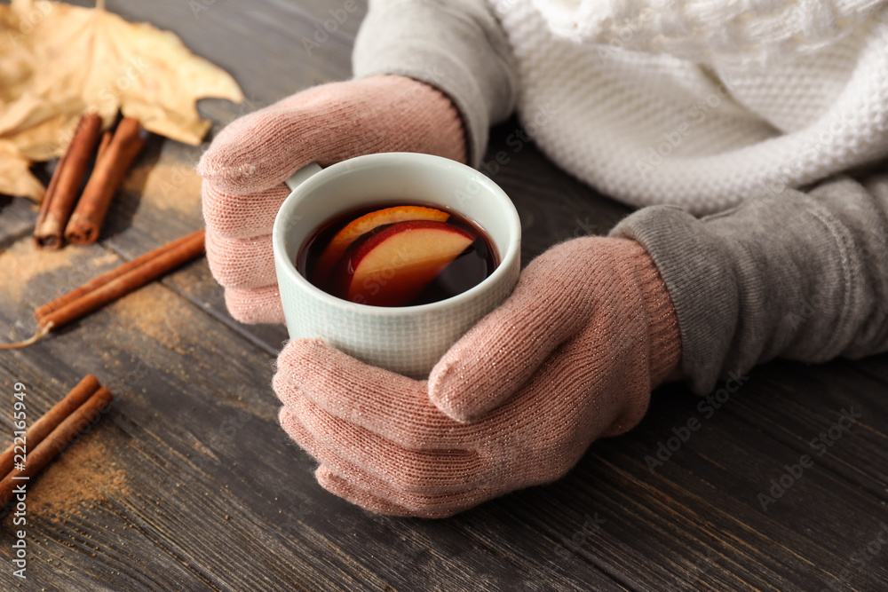 Wall mural woman holding cup of delicious mulled wine on wooden table, closeup