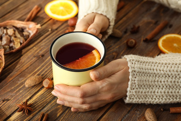 Woman holding metal cup of delicious mulled wine on wooden table, closeup