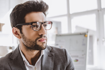 portrait of handsome businessman in glasses looking away in office