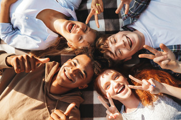 Image of happy young friends men and women laughing, and lying on blanket in circle