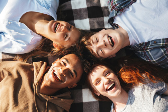 Portrait of happy people men and women laughing, and lying on blanket in circle outdoor