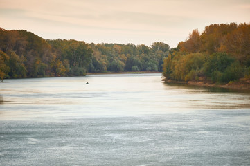fisherman on a boat fishing in the river, autumn forest and cloudy sky
