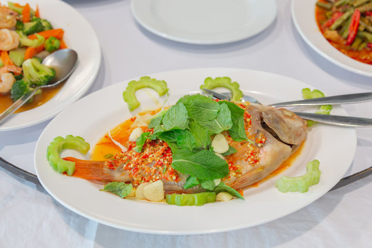 Fried fish topped with fresh herbs and sweet spicy sauce on plate.Thai Food