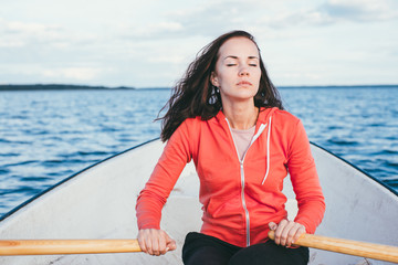 amazing beautiful haired girl swims on a wooden boat and rowing with oars in the gorgeous spring lake. Lifestyle without makeup