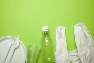 Plastic disposable utensils on green background. fork, knives, plates, cups and bottle,  bag