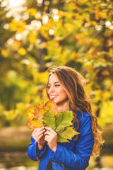 Cute smiley woman holding autumn leafs in the nature.