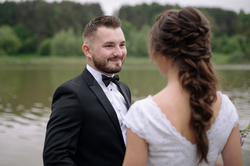 Smiling groom and bride in beautiful wedding dress standing on the pier near the lake. Wedding couple