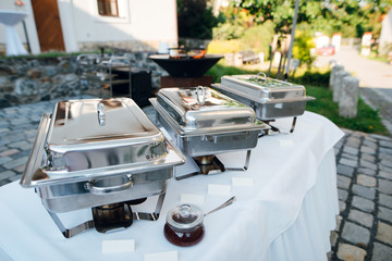 Wedding buffet table with row of hot food service steam pans. Outdoors in the garden