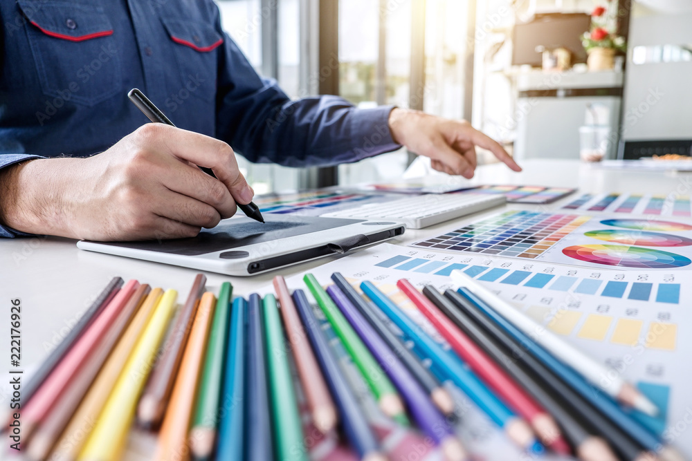 Poster Image of male creative graphic designer working on color selection and drawing on graphics tablet at workplace with work tools and accessories