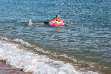 a man swims in a pink rubber ring in the sea