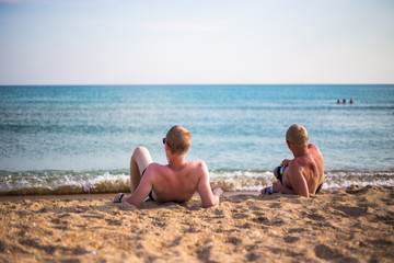 two men resting on the sand by the sea