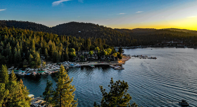Aerial sunset view of Lake Arrowhead with blue water, green trees, boats, golden clouds, yellow, red, orange, blue, pink, purple colors