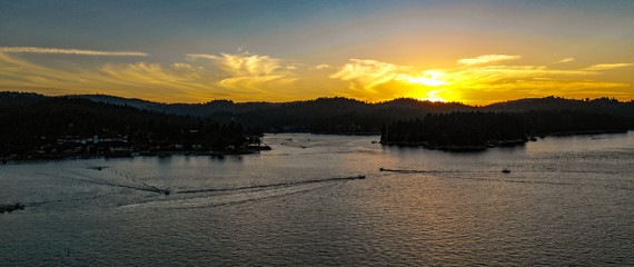 Aerial sunset view of Lake Arrowhead with blue water, green trees, boats, golden clouds, yellow, red, orange, blue, pink, purple colors