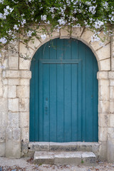 Old blue green door in a stone wall with flowers above.