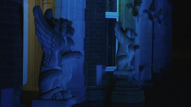 A gothic style stone gargoyle statue lit up by coloured lights.