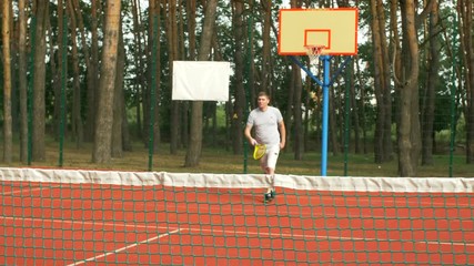 Active healhty lifstyle millennial man in sports clothing playing tennis game on hardcourt. Positive amateur tennis player hitting ball with different grip techniques during training session outdoors.