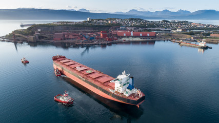 Aerial shot of a cargo ship approaching port terminal with help of towing ship, Narvik, Norway