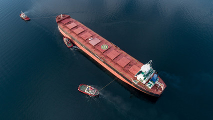 Aerial shot of a cargo ship approaching port with help of towing ship