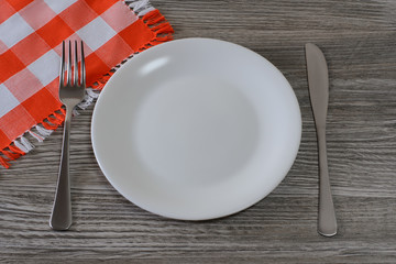 Empty white round plate, knife, fork and tablecloth on  wooden table. Top view photo