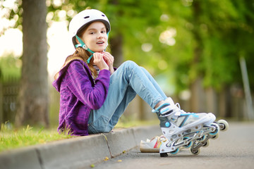 Pretty little girl learning to roller skate on summer day in a park. Child wearing safety helmet...